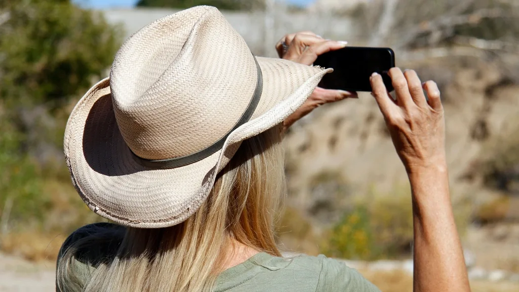 A person in a sun hat holding up a phone outdoors